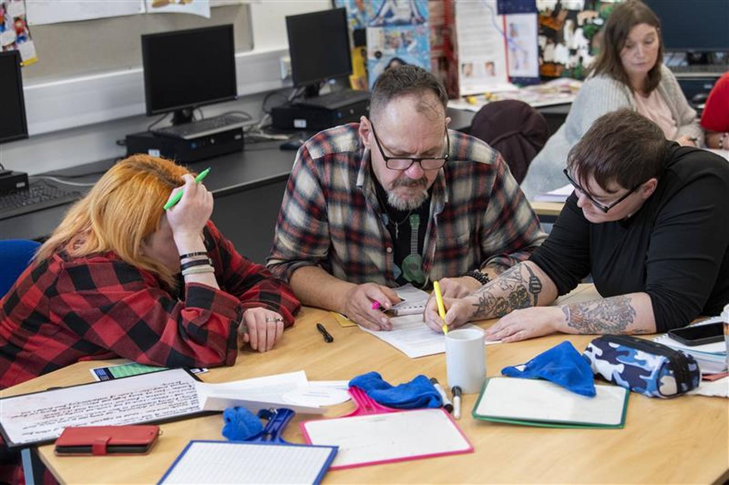 A group of adults in a classroom setting, engaged in a collaborative learning activity, writing and discussing at a table with papers and stationery.