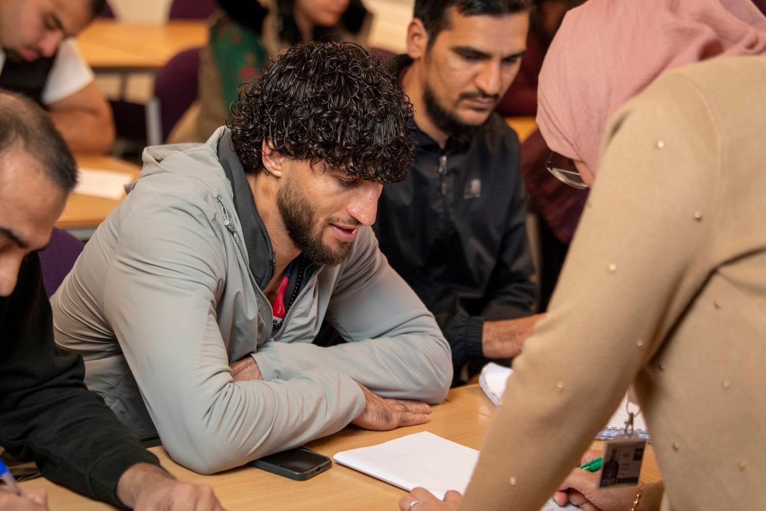 A group of students sitting at a table, taking notes in a classroom setting.