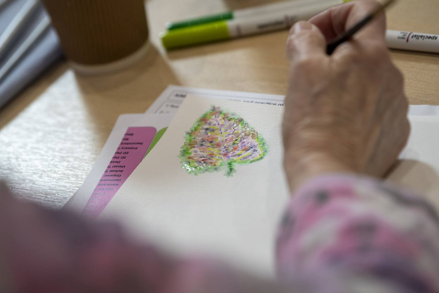 A person colouring a Christmas tree with multi-coloured pens on a piece of paper.