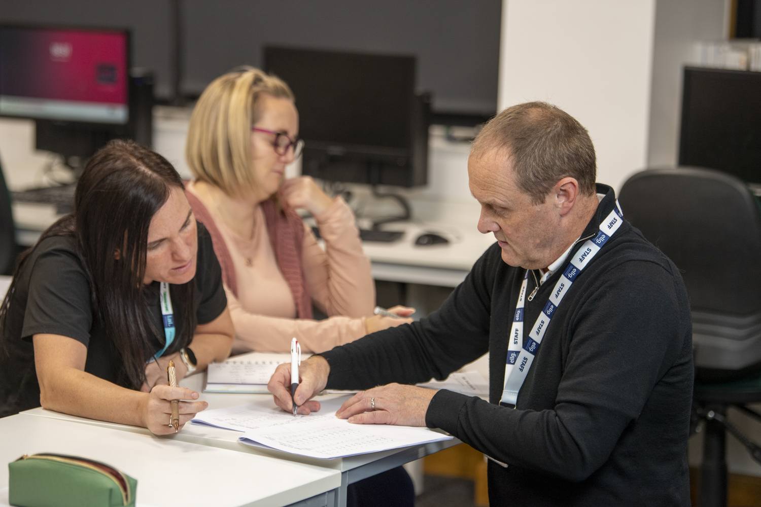 A man and two women in a college office, with the man signing a document and the women observing.