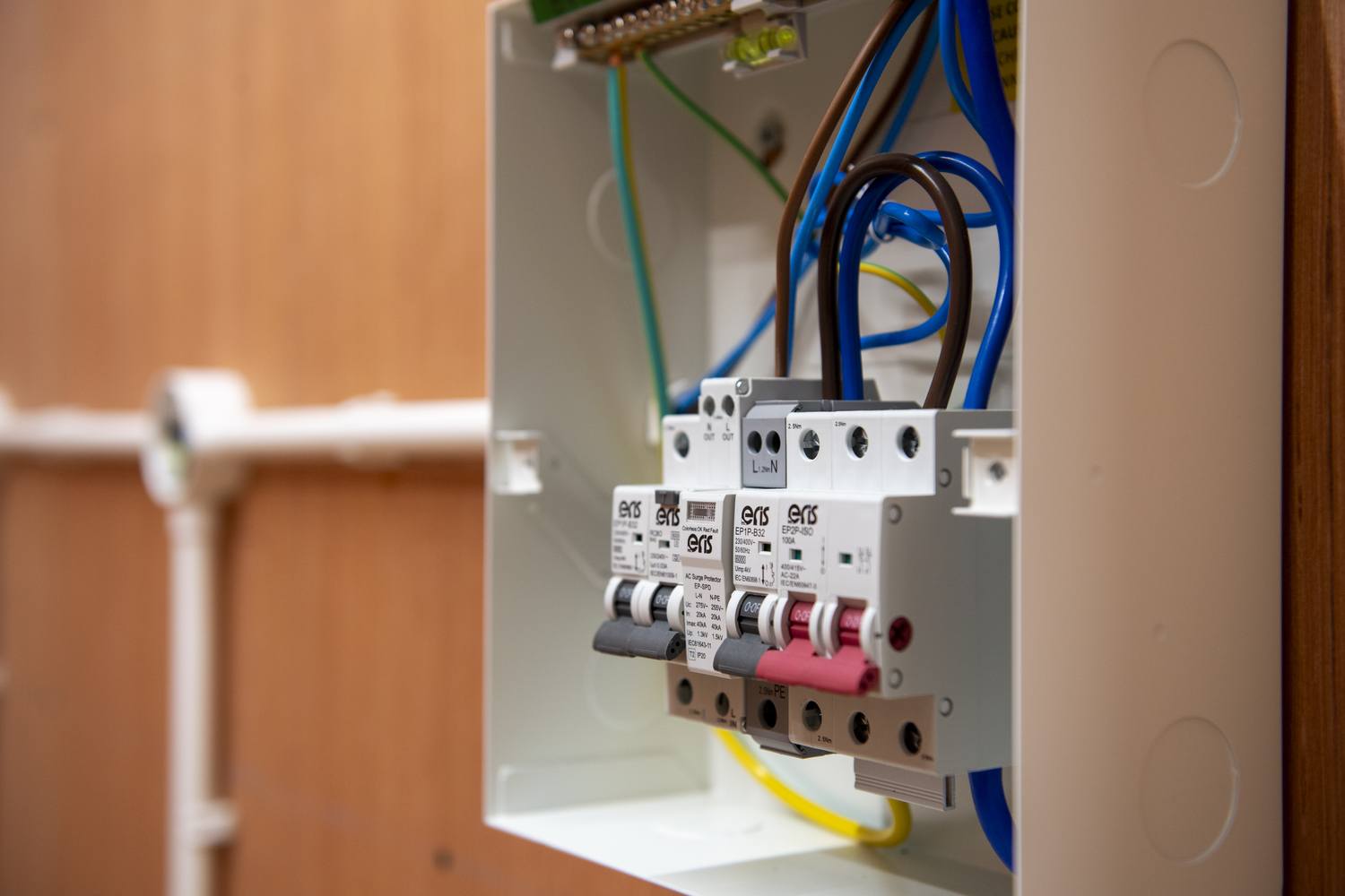 Three electrical circuit breakers in a metal box with blue, brown, and yellow wires. Labels include Eaton and 20A. Mounted on a wooden wall.