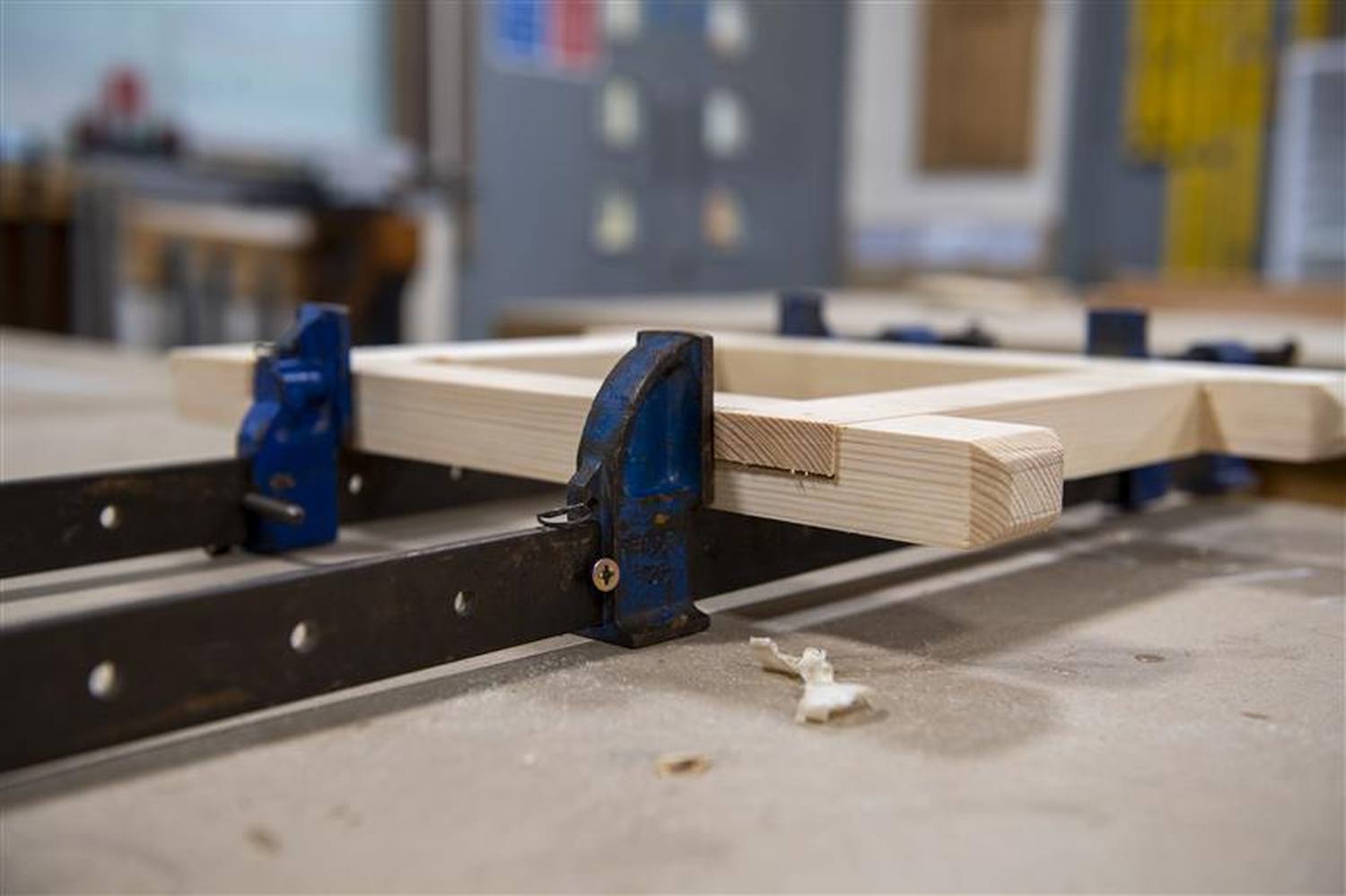 Two pieces of wood clamped together on a black metal workbench in a workshop.