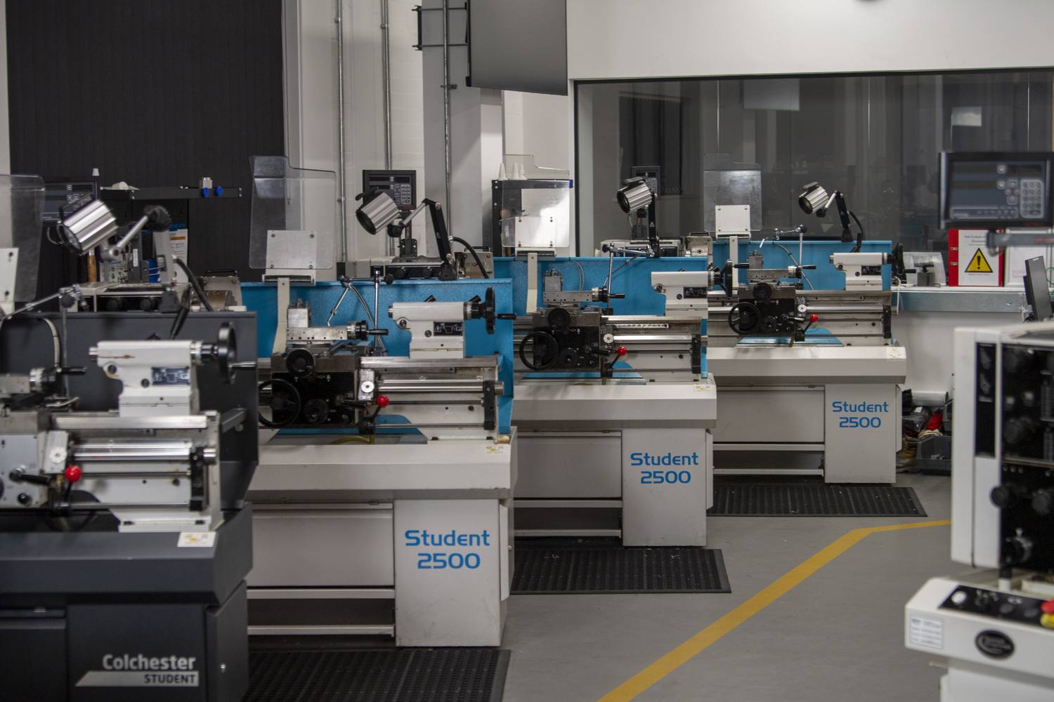 A college workshop with several Colchester Student 2500 lathes, equipped with protective shields and control panels, arranged in rows for machining training.