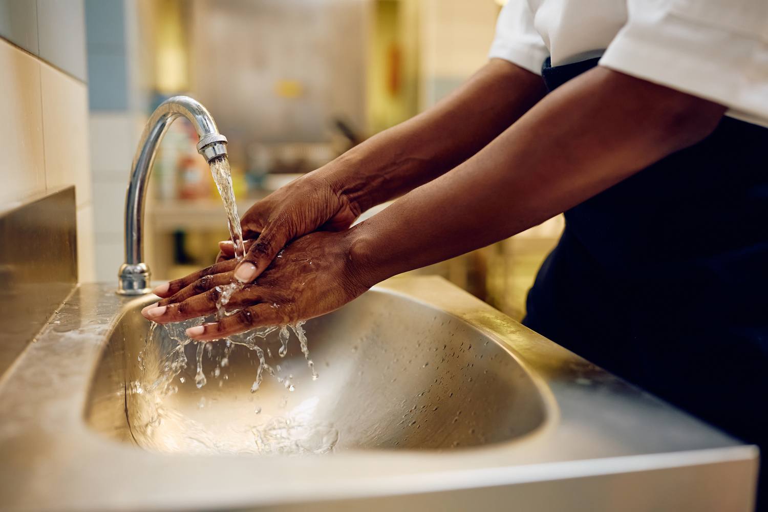 A person washing their hands under a running tap in a kitchen sink, emphasising hygiene practices.