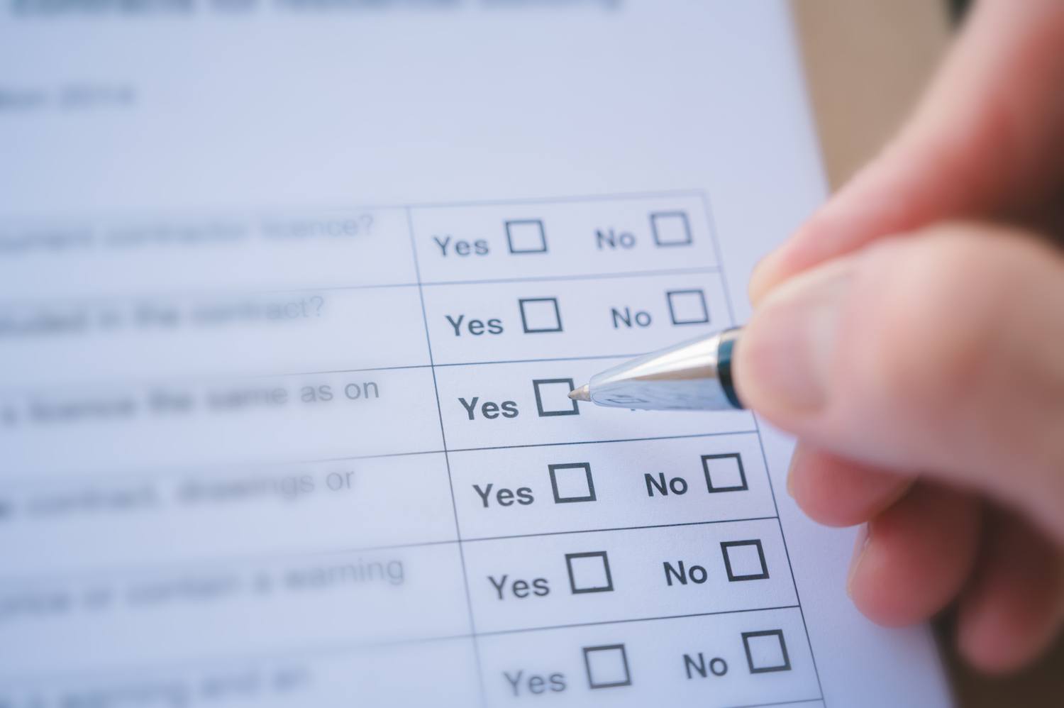 A hand holding a pen filling in a Yes or No checkbox on a printed form.