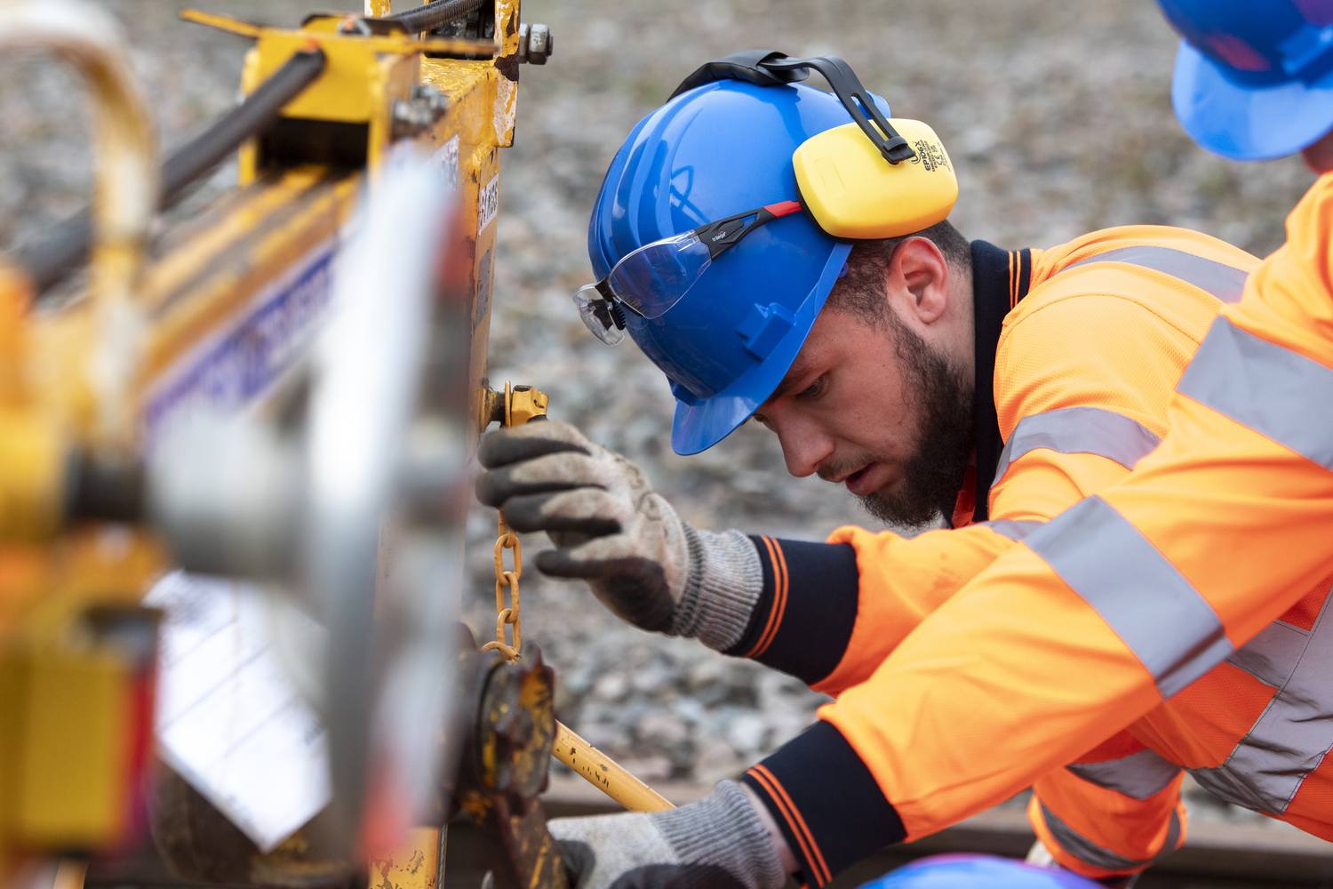 Construction worker in high-visibility clothing and hard hat using a hammer on a metal structure, emphasising safety and practical skills in engineering education.